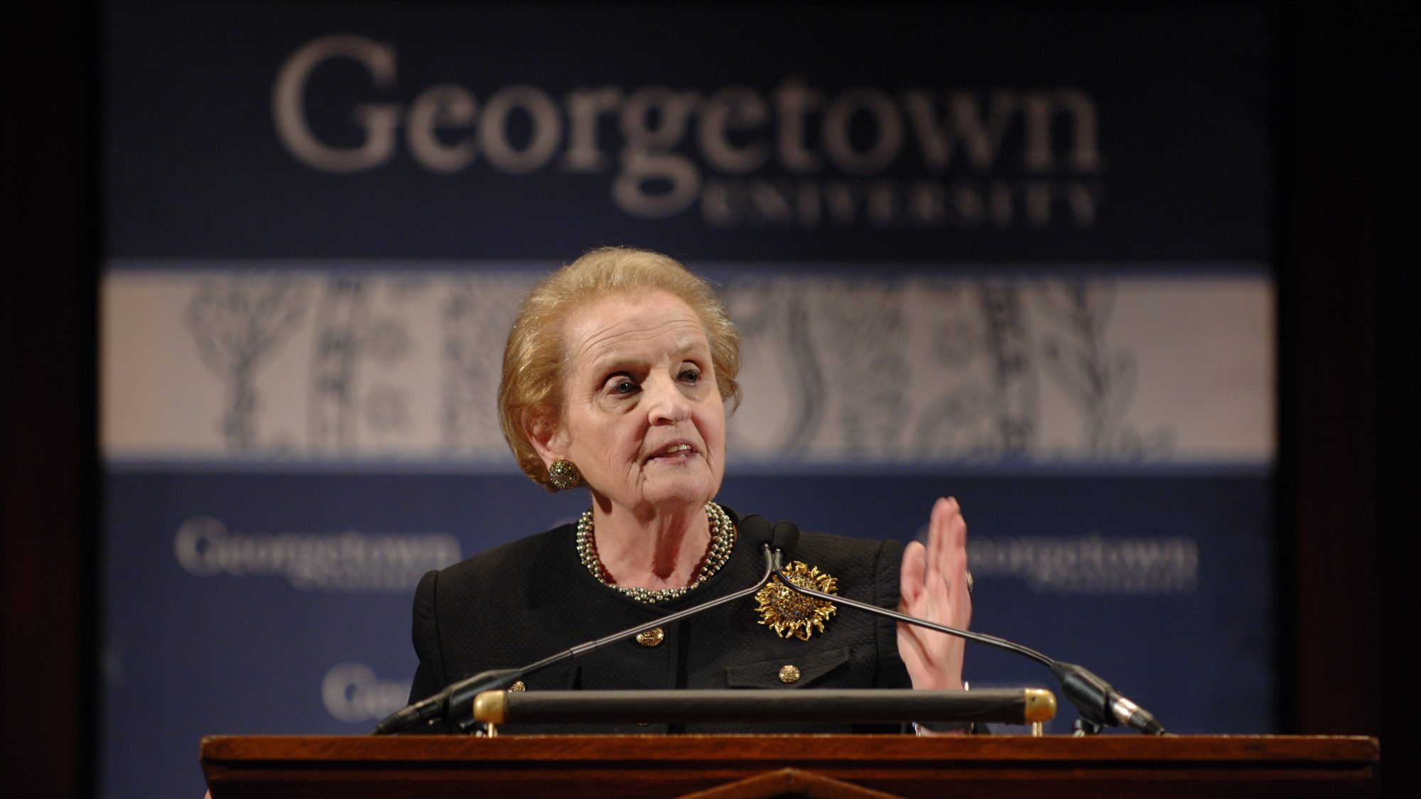 Madeleine Albright speaks behind a podium with a 