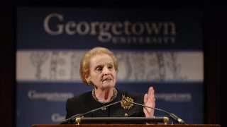 Madeleine Albright speaks behind a podium with a 