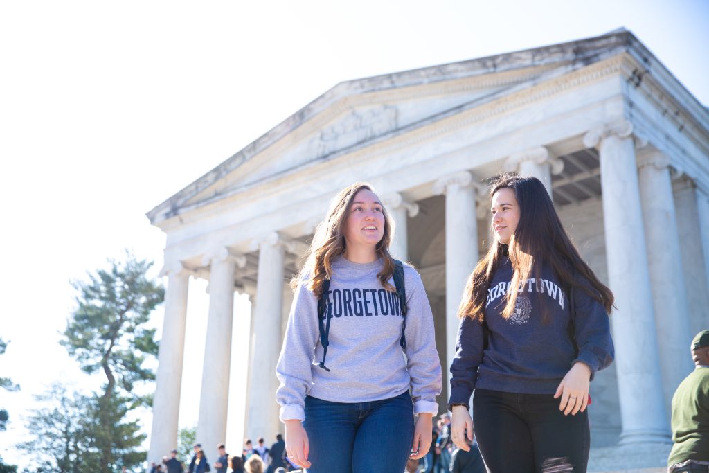 Two Georgetown students wearing Georgetown sweatshirts walk in front of the Lincoln Memorial