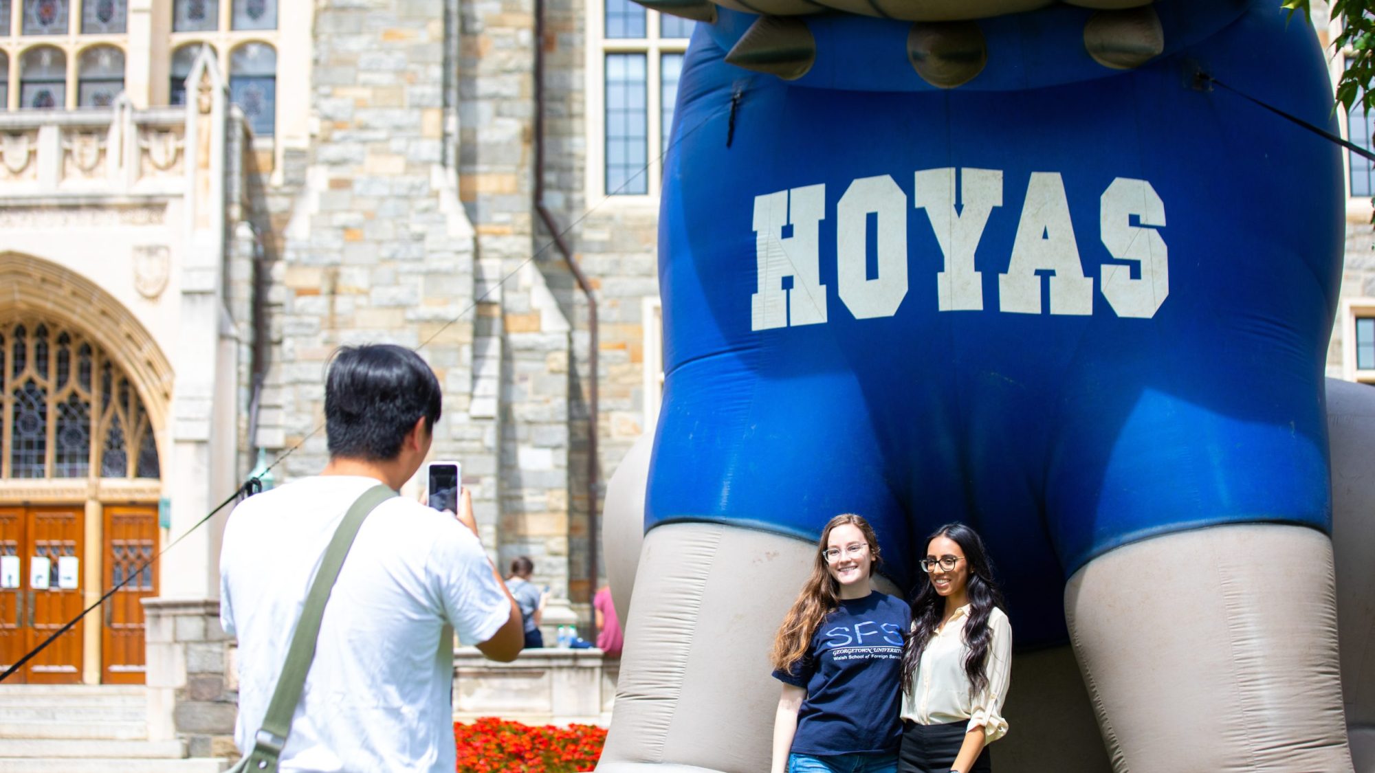 A person takes a photo of two students in front of the blowup Jack the Bulldog