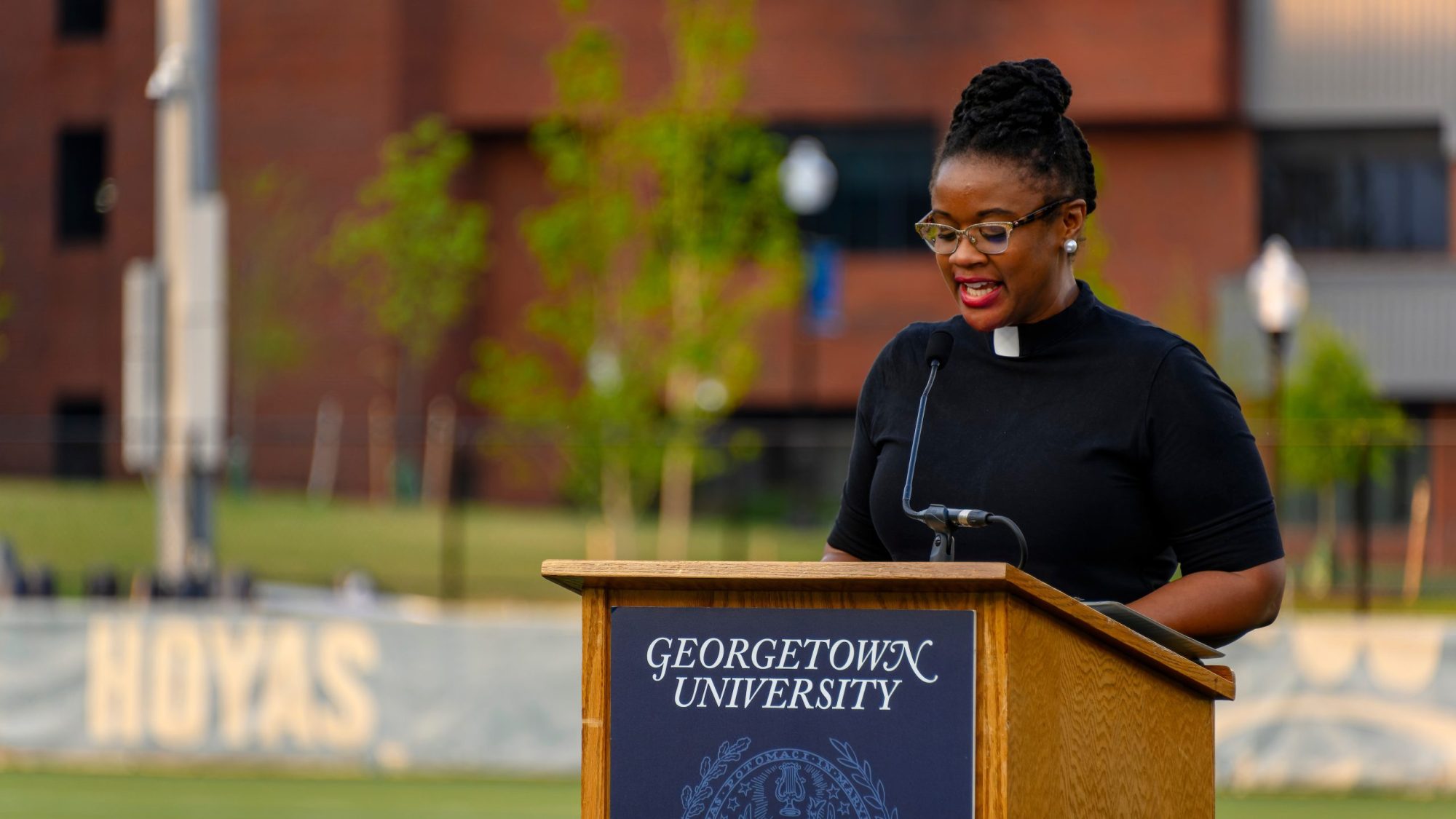 Rev. Ebony Grisom wears a collar and speaks from behind a podium in a field