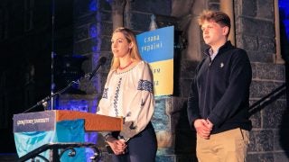 Two students speak from behind a podium with the Ukrainian flag across the front