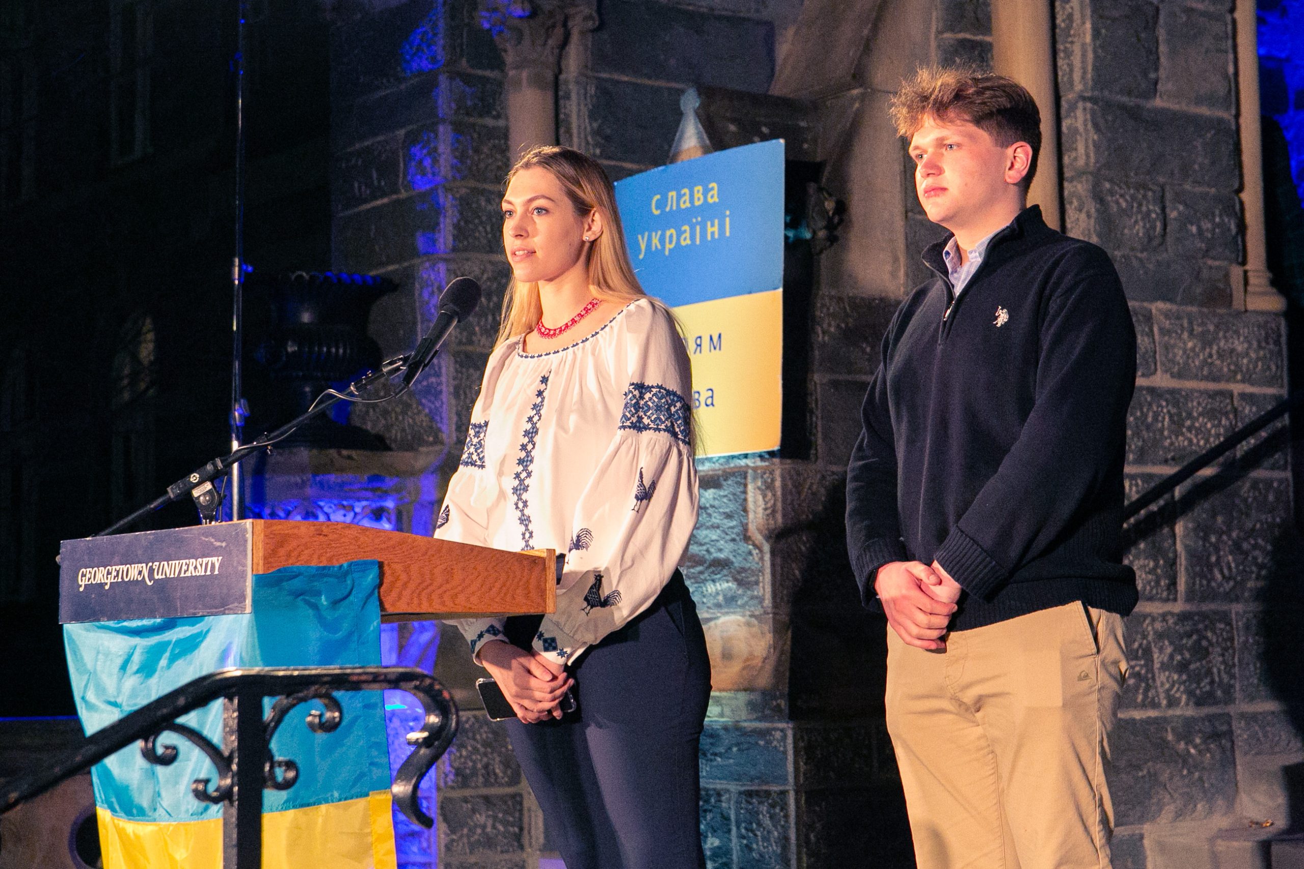 Two students speak from behind a podium with the Ukrainian flag across the front