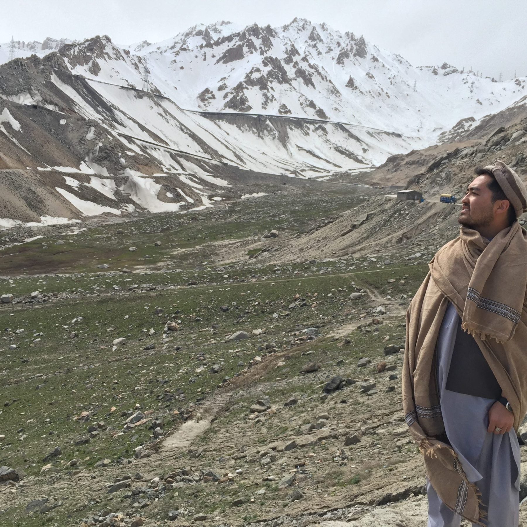 Shuja wears traditional Afghan clothing with snow-capped mountains in the background