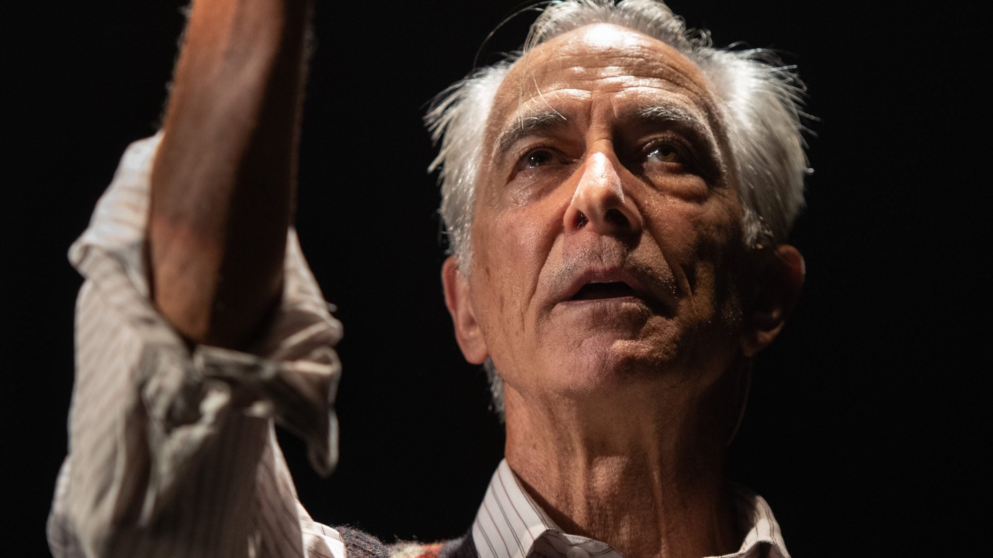 David Strathairn portrays Jan Karski, looking up at raised hand in knit sweater vest.