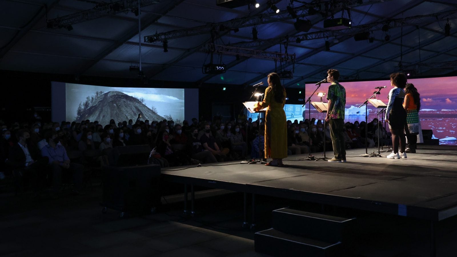 Actors perform on a stage with a projection of mountains behind the audience