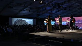 Actors perform on a stage with a projection of mountains behind the audience