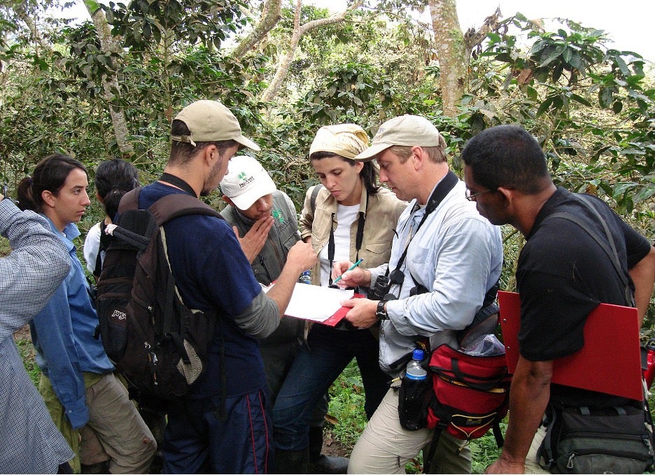 Marra stands surrounded by trees talking to an attentive group of people