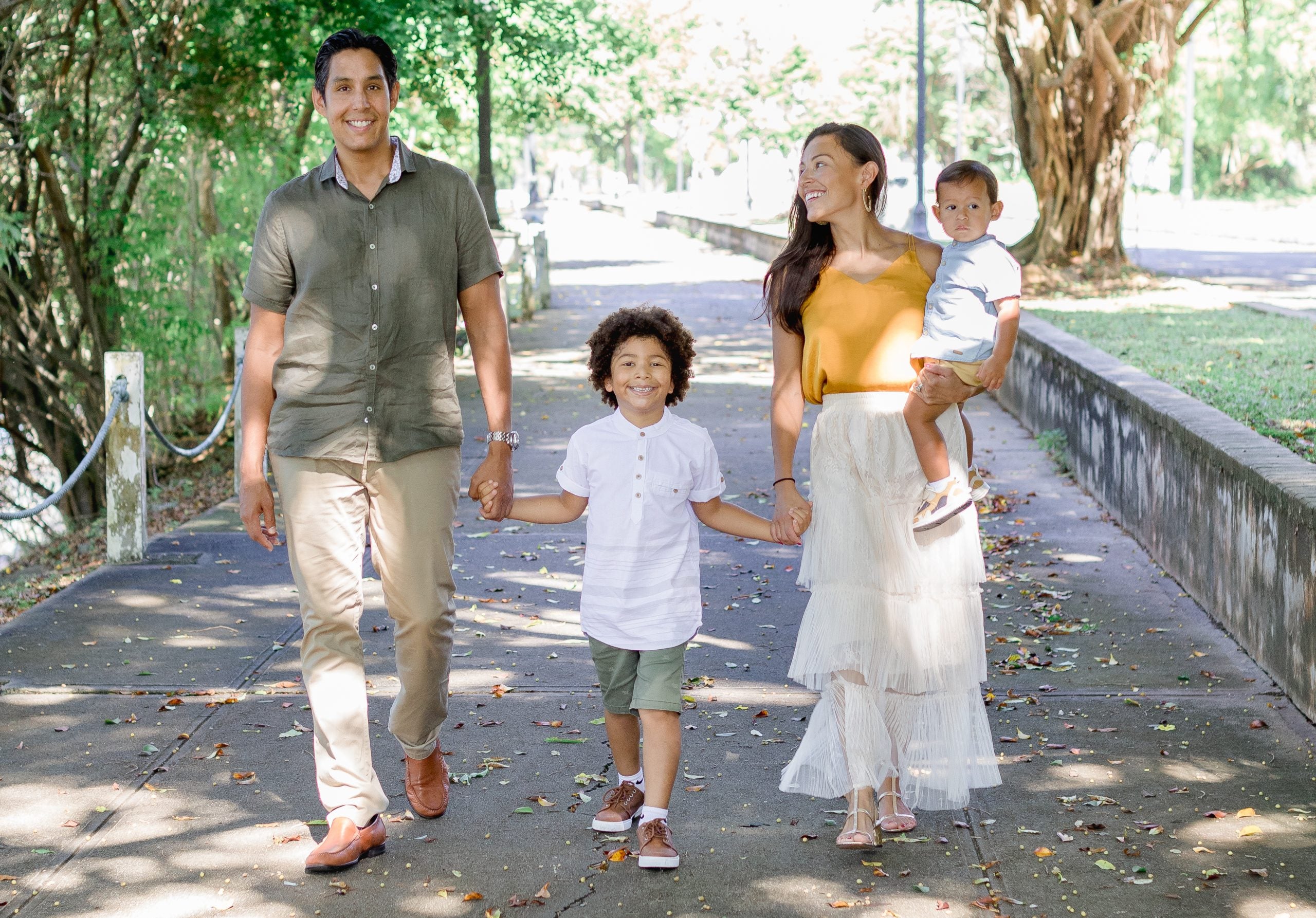 A man walks next to his son next to his wife holding their baby in a park outside