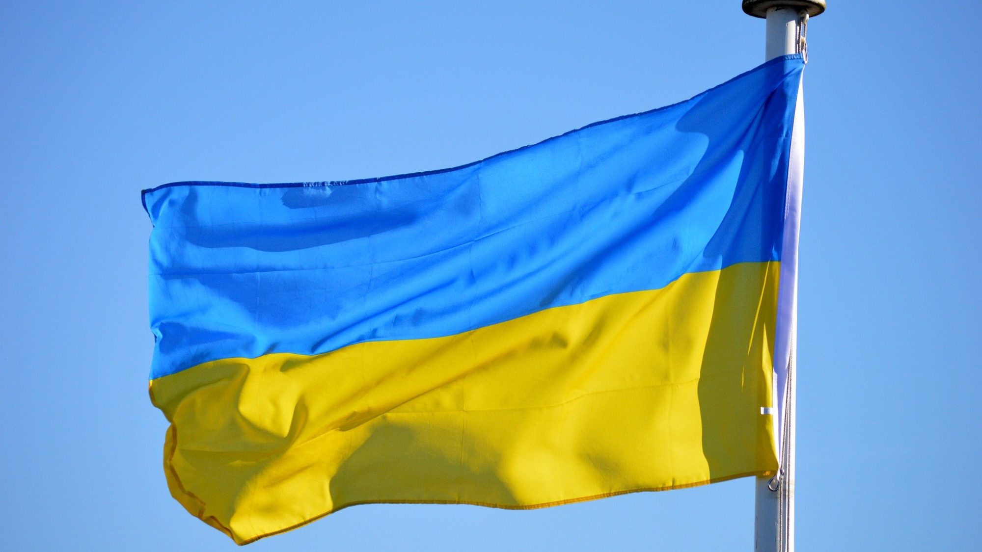 Ukraine flag on pole in front of blue sky.