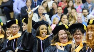 Student wearing graduation attire holding a diploma cheers in a crowd