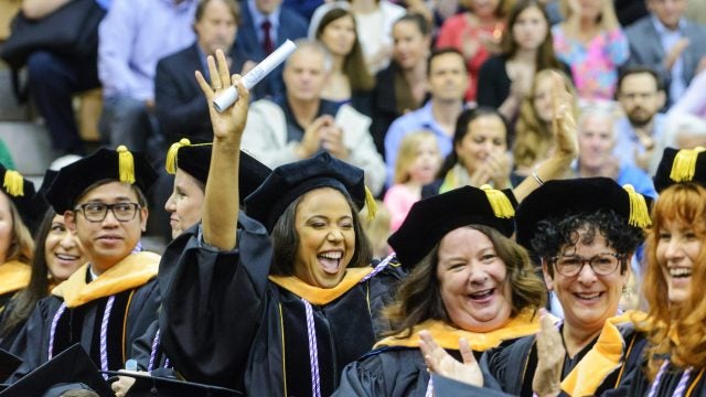 Student wearing graduation attire holding a diploma cheers in a crowd