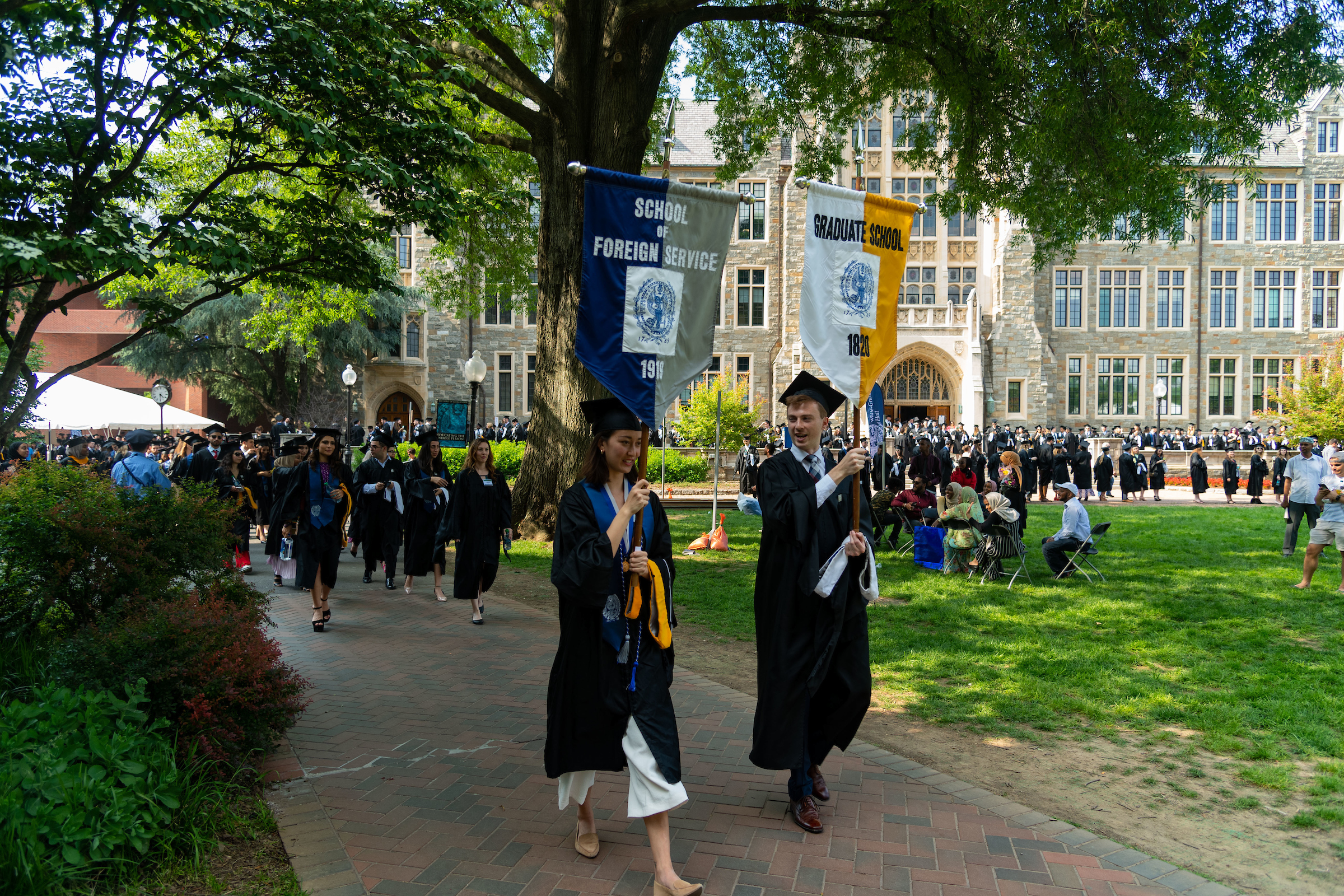 Students in caps and gowns holding "School of Foreign Service" and "Graduate School of Arts & Sciences" banners