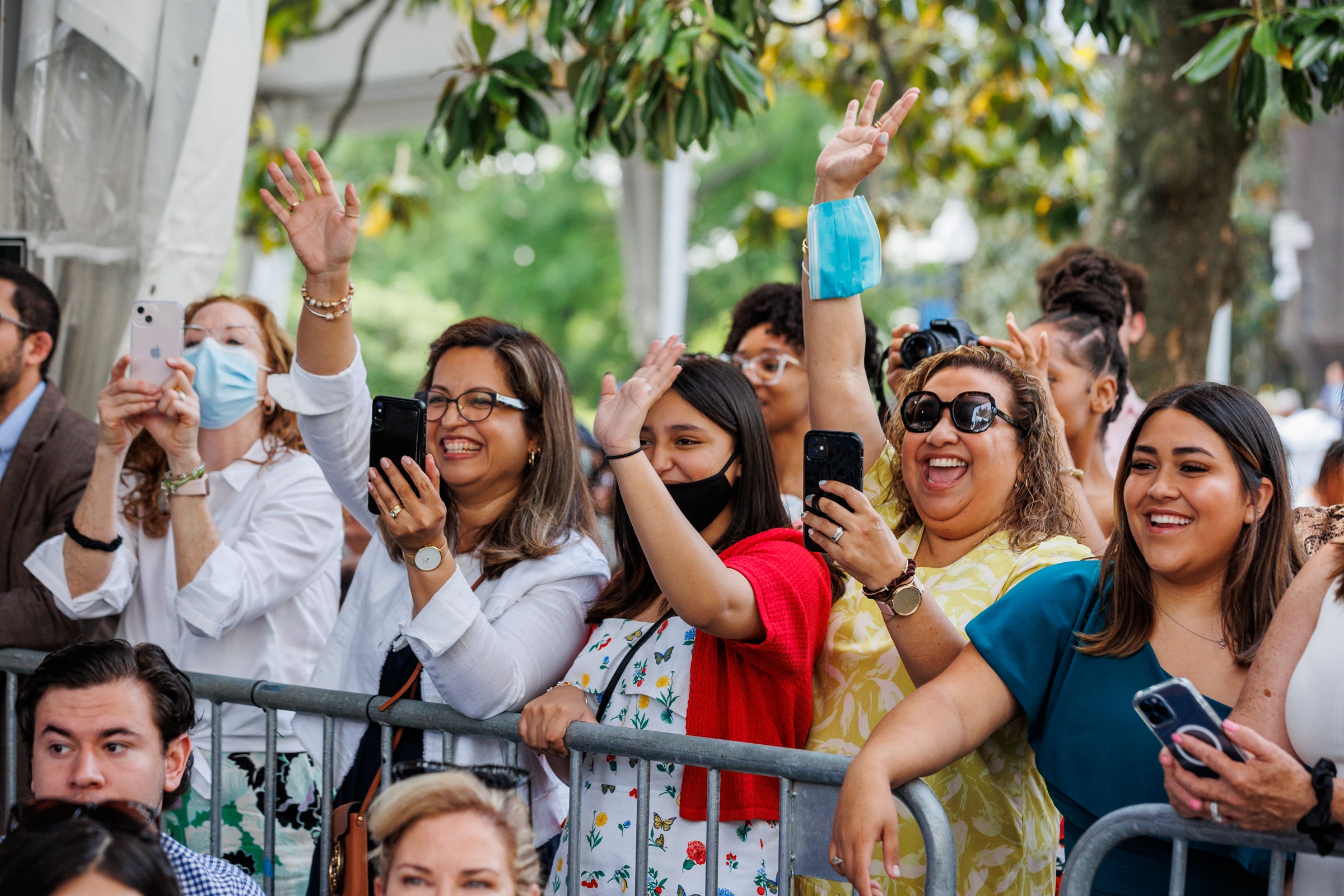 Parents hold cell phones and wave to graduating students