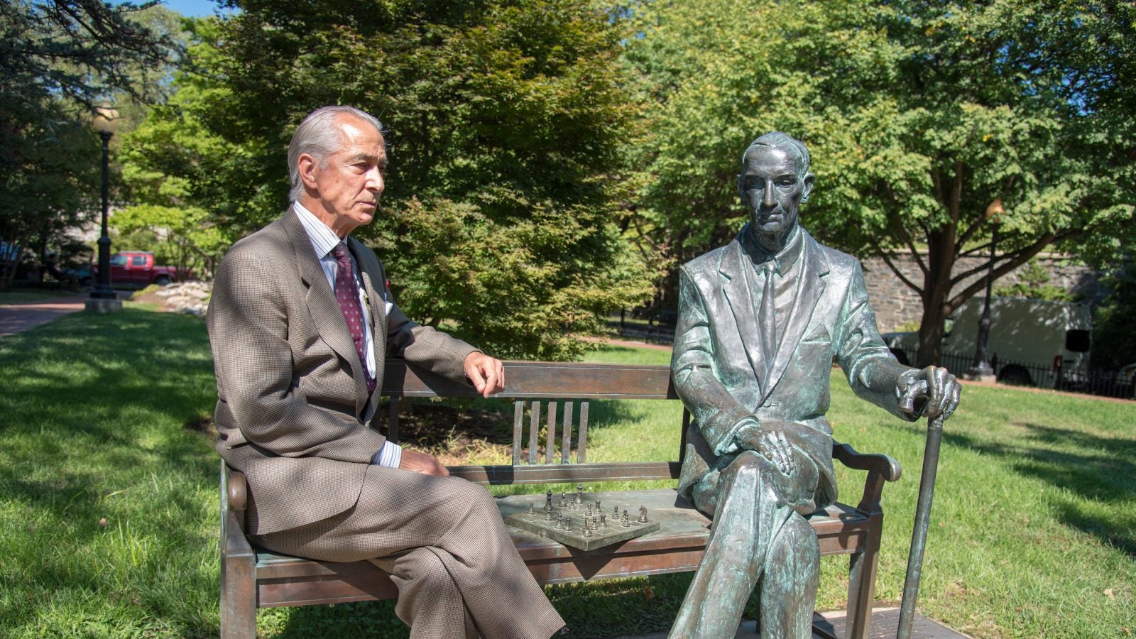 Strathairn as Karski sits on a bench next to a greening Karski statue with a cane