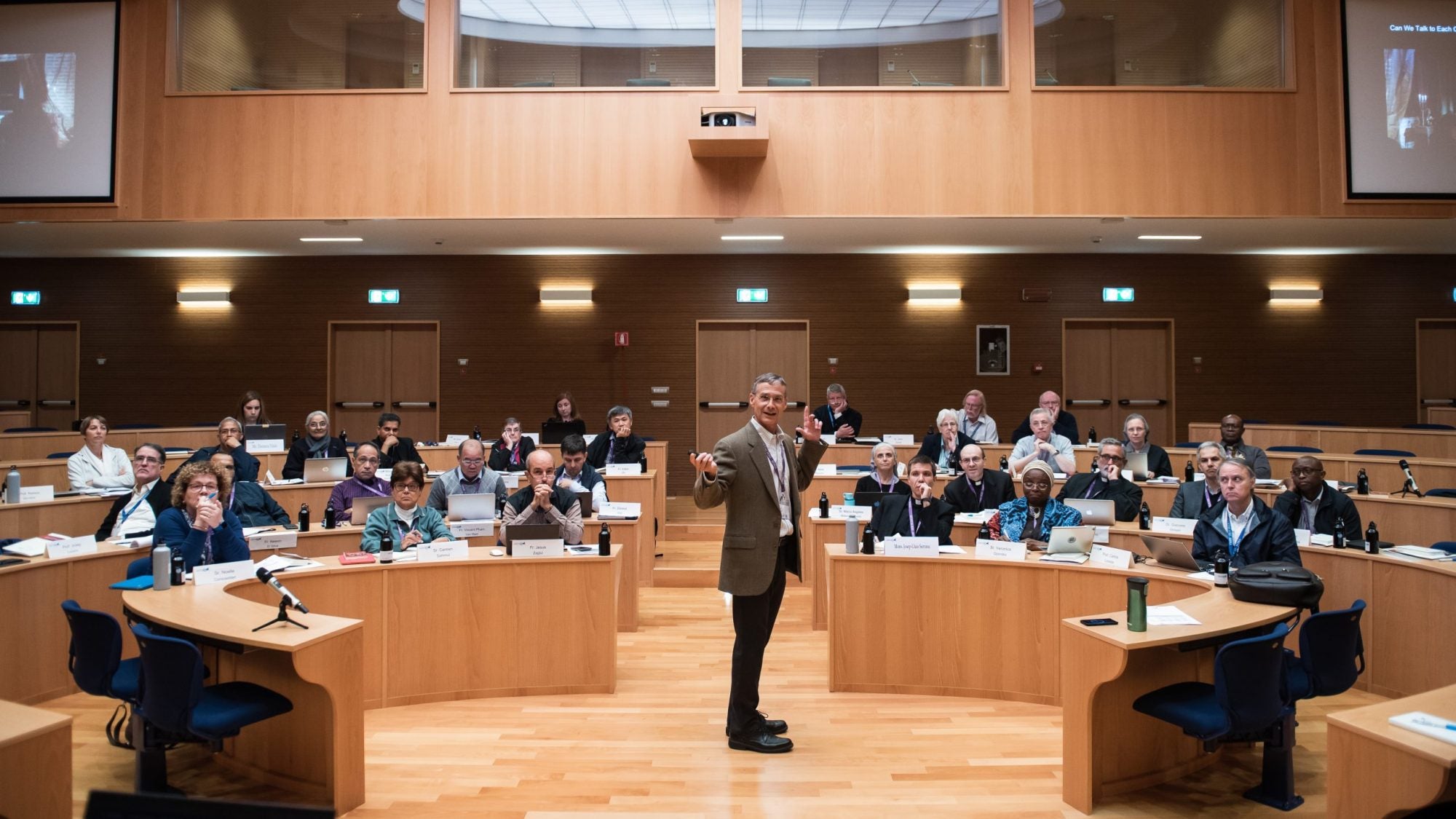 Professor in the middle of a lecture turns to face the camera as adult students watch