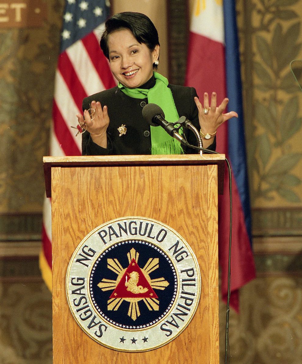 Gloria Macapagal-Arroyo stands behind a podium in front of American and Filipino flags