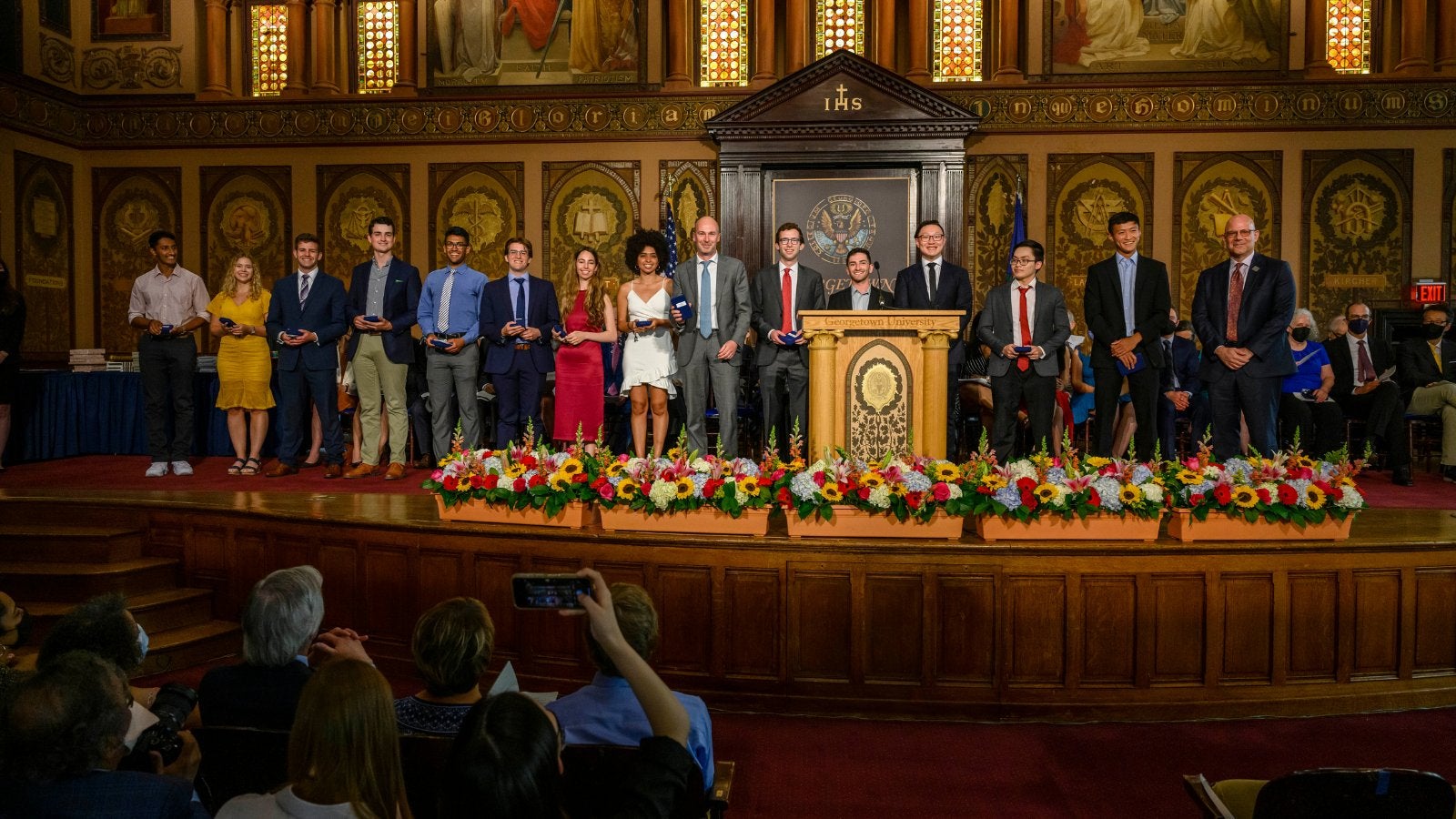 A group of students stand on stage in Gaston Hall during the School of Foreign Service's Tropaia undergraduate awards ceremony. 