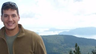 An image of Austin Tice, a law student at Georgetown, standing in front of a mountain wearing a brown jacket with sunglasses on his head.