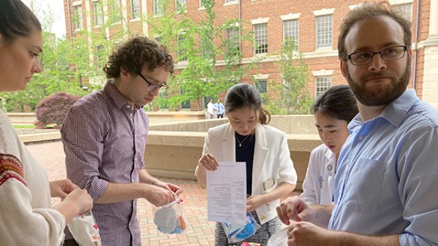 Four medical students assemble first aid kits on a table outside.