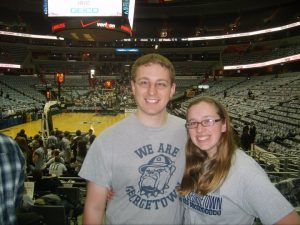 A blonde man and blonde woman with glasses wears "We Are Georgetown" gray t-shirts at a basketball game