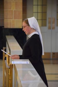 Allison wears a white habit and black dress and prays in front of an alter