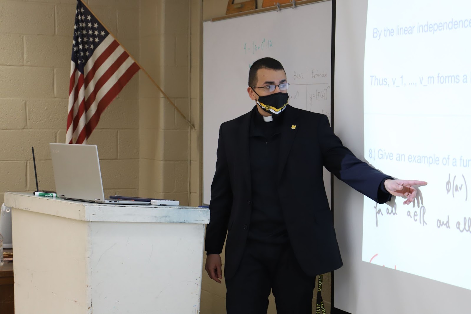 Christian Verghese points to a projection while teaching in a classroom in front of an American flag