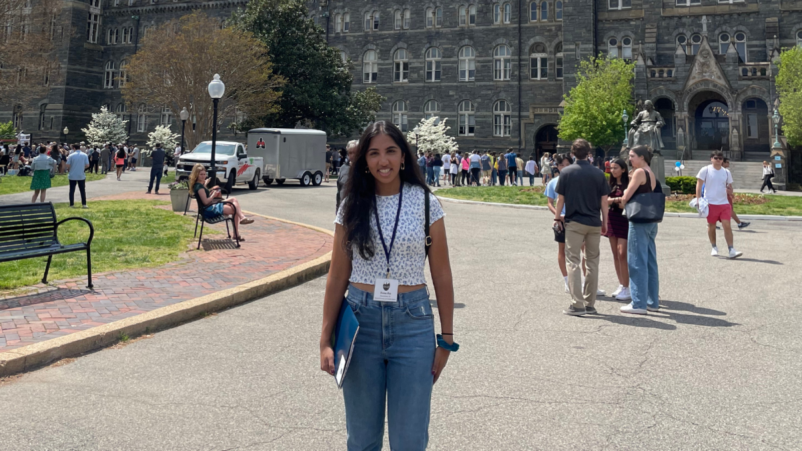 An image of Roma Jha, an incoming student, wearing a T-shirt and jeans and standing in front of Healy Hall, a historic building on Georgetown's campus.