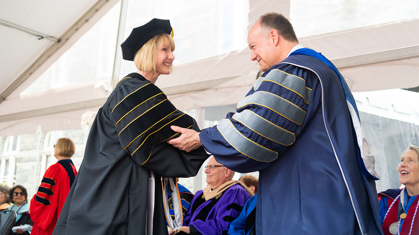 A graduate of a Ph.D. program wearing a cap and gown shakes the hand of Georgetown University President John J. DeGioia at a commencement event in 2022.
