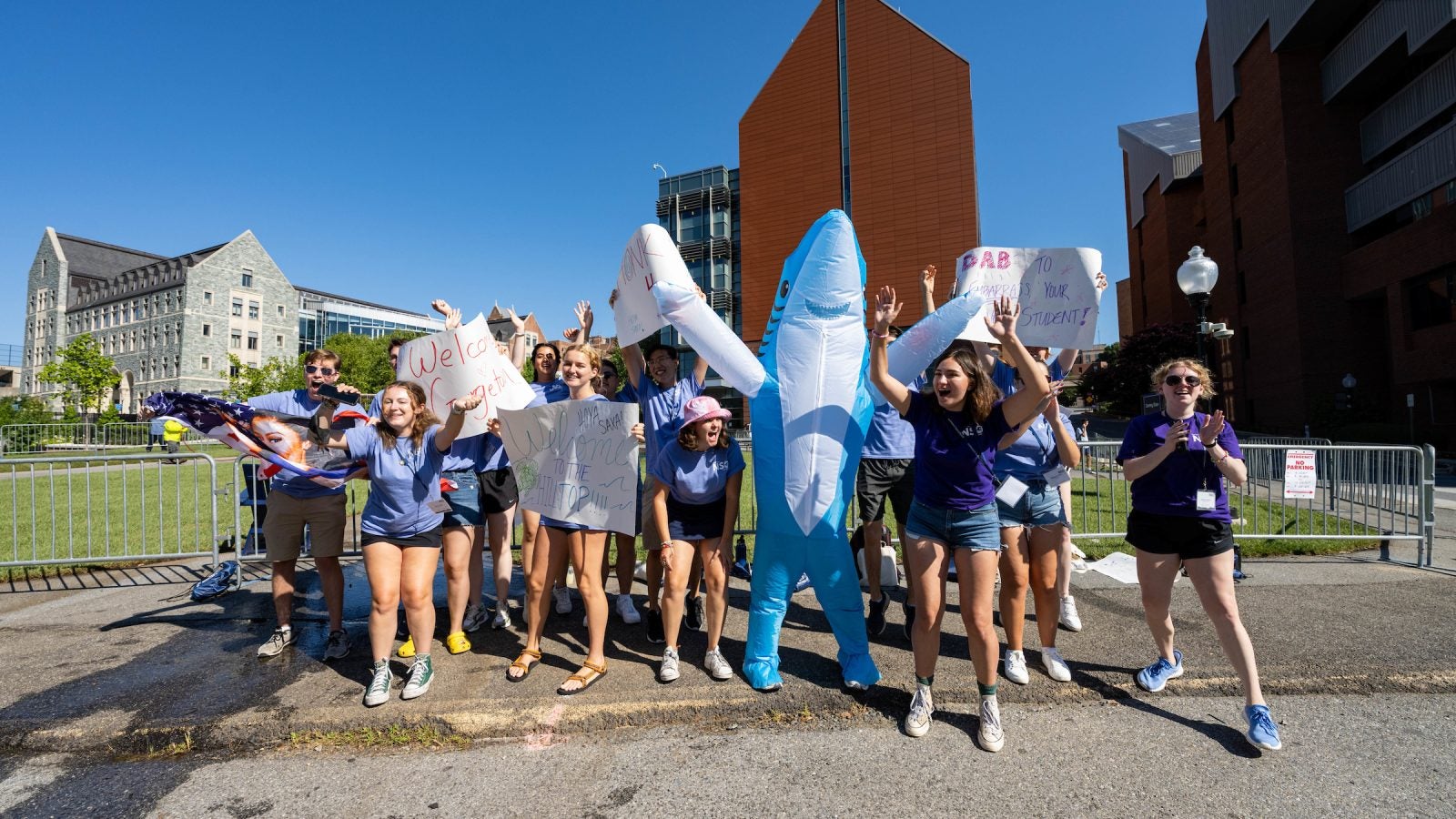 Students in matching T-shirts and one dressed as a shark hold signs and cheer