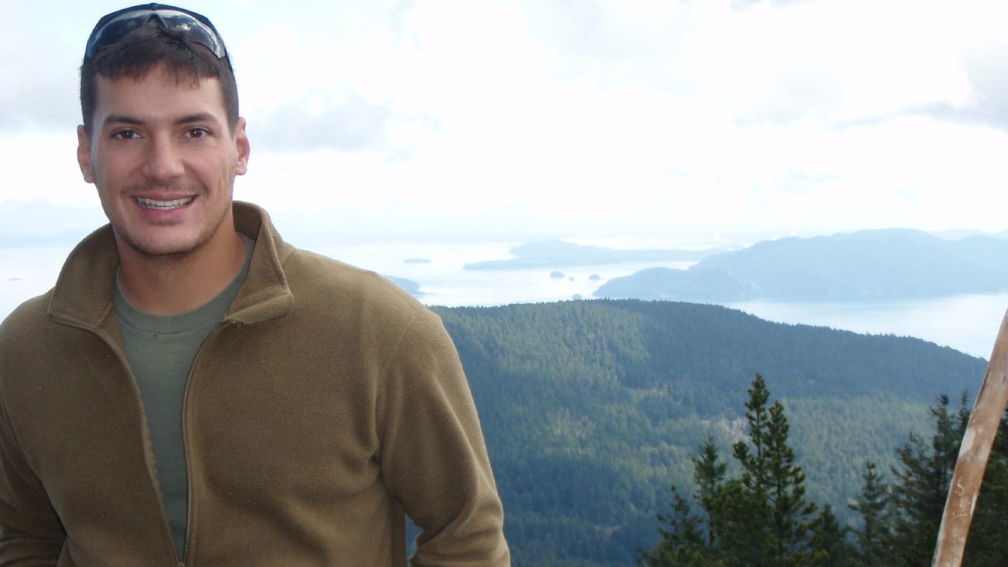Austin Tice wears a dark khaki-colored zip up in front of mountains