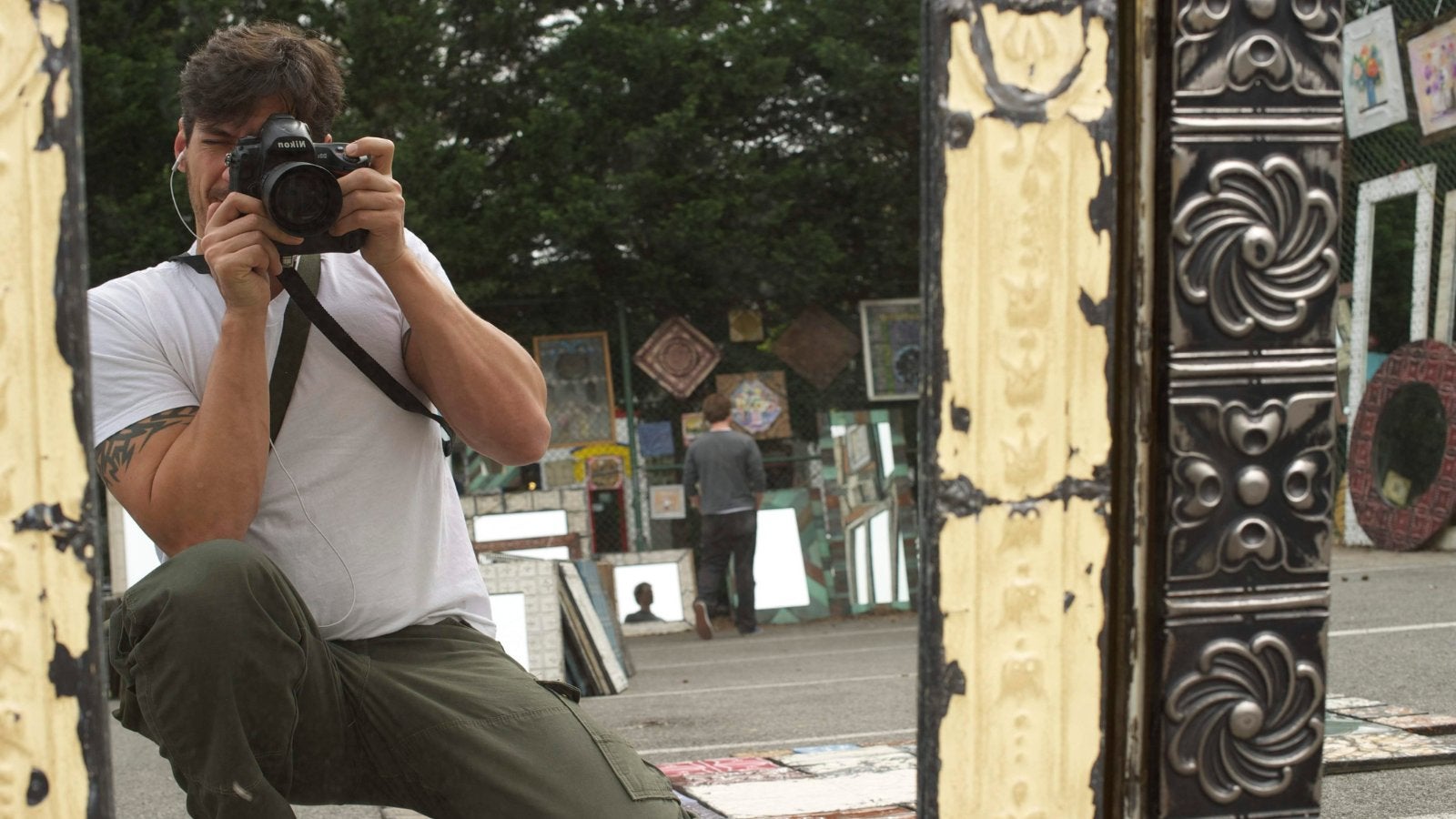 Man taking a photo with the camera in front of his face across the street from art vendors