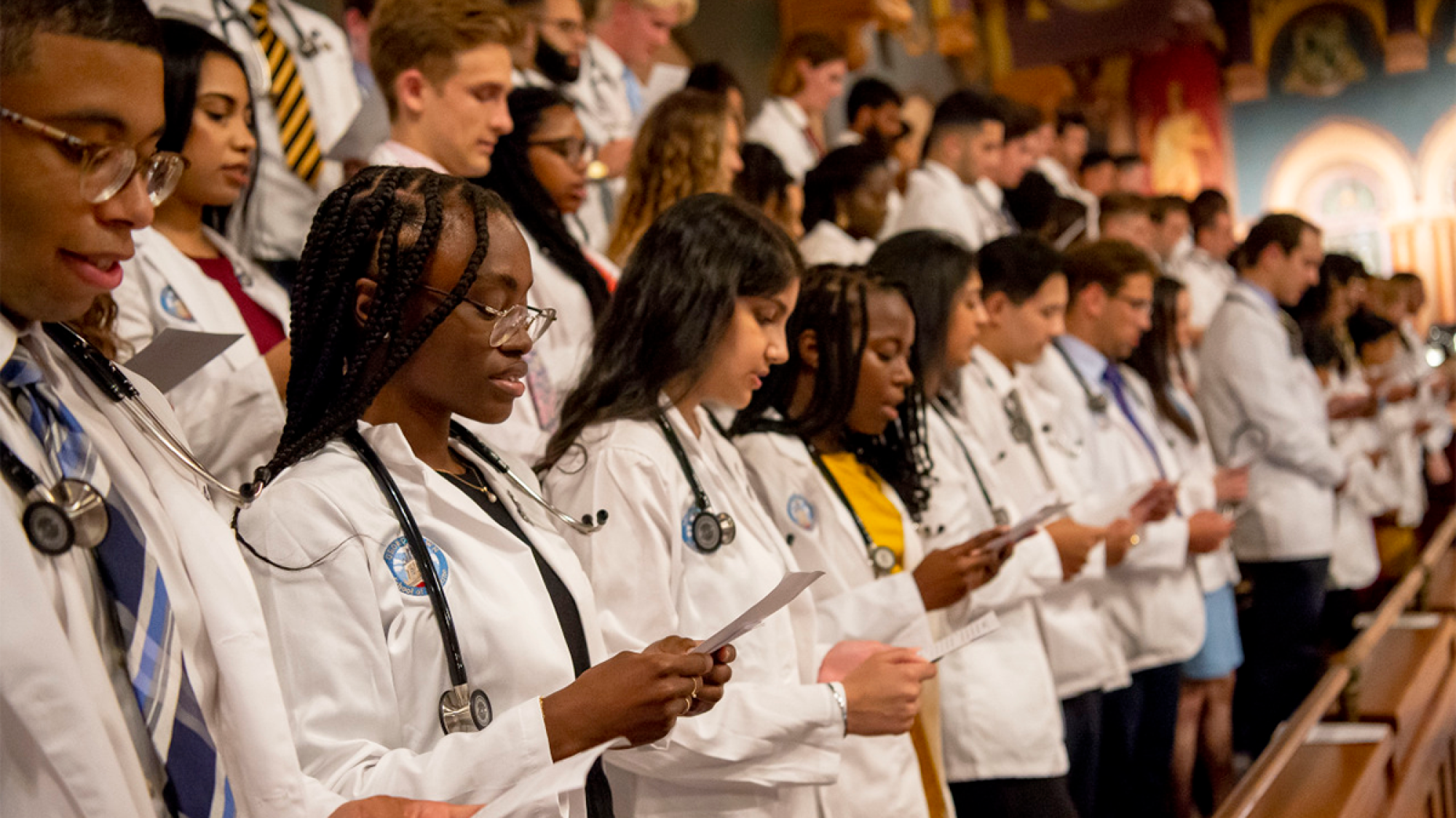 A group of first-year medical students read the Hippocratic Oath at Georgetown&#039;s annual White Coat Ceremony in Gaston Hall.