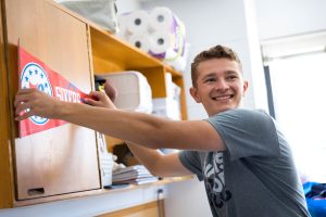 John Breitfelder (B'26) holds up a Philadelphia 76ers red flag in his dorm room as he unpacks during move-in 2022.