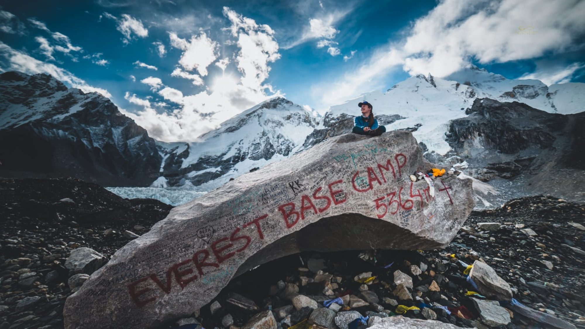 An image of Sarah Watson sitting on top of a rock with mountains in the background at Mt. Everest base camp in Nepal.
