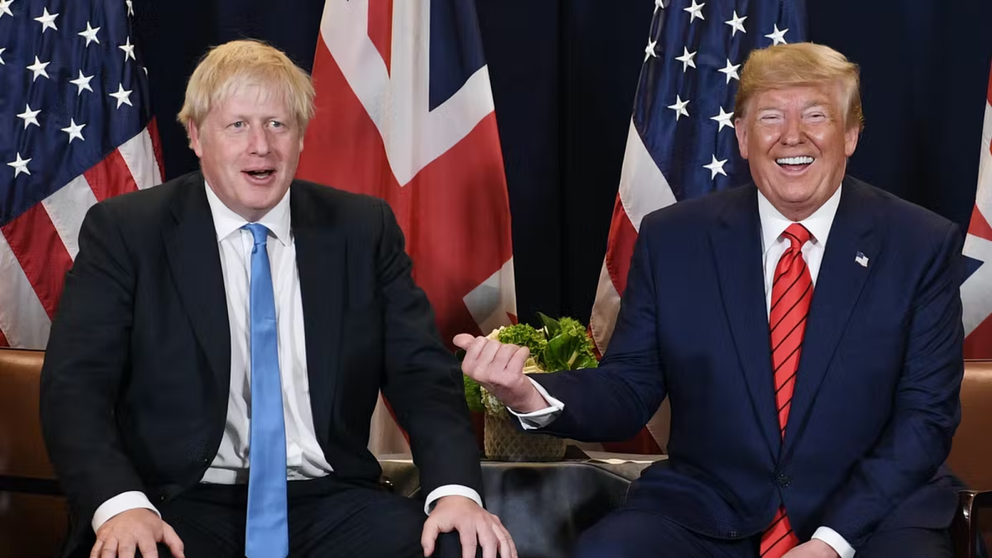 Boris Johnson seated next to Donald Trump, in front of UK and US flags.