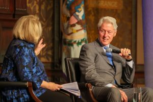 Bill Clinton speaks into a microphone while Melanne Verveer asks him a question