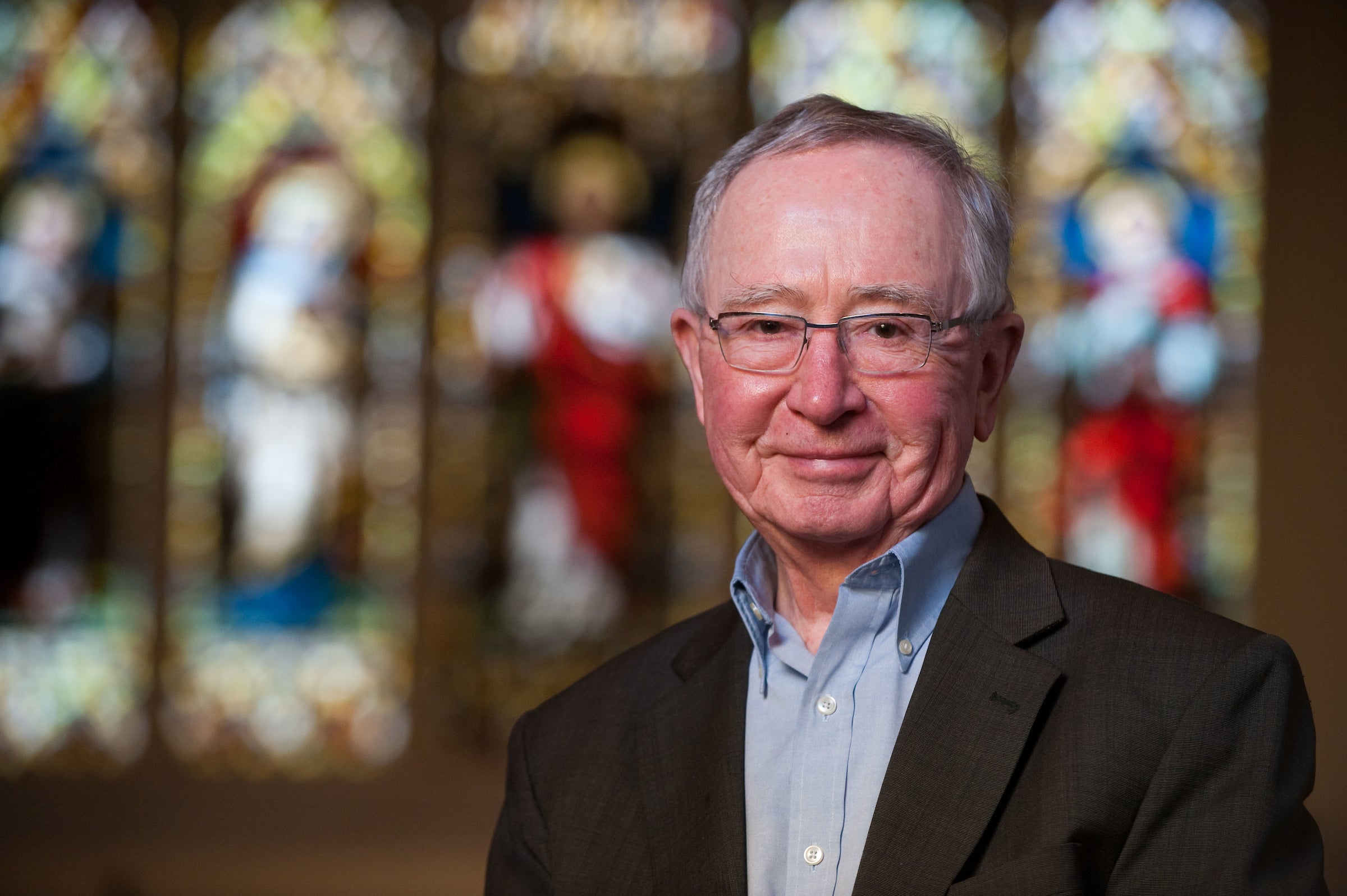 Fr. O'Malley takes a headshot in front of glass windows