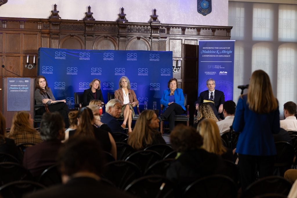 A woman with her back to the camera asks questions of the panel from a microphone in the aisle of the audience.