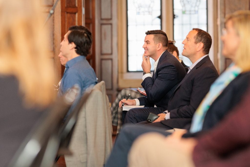 A young man leans forward and smiles while in an audience of a panel.