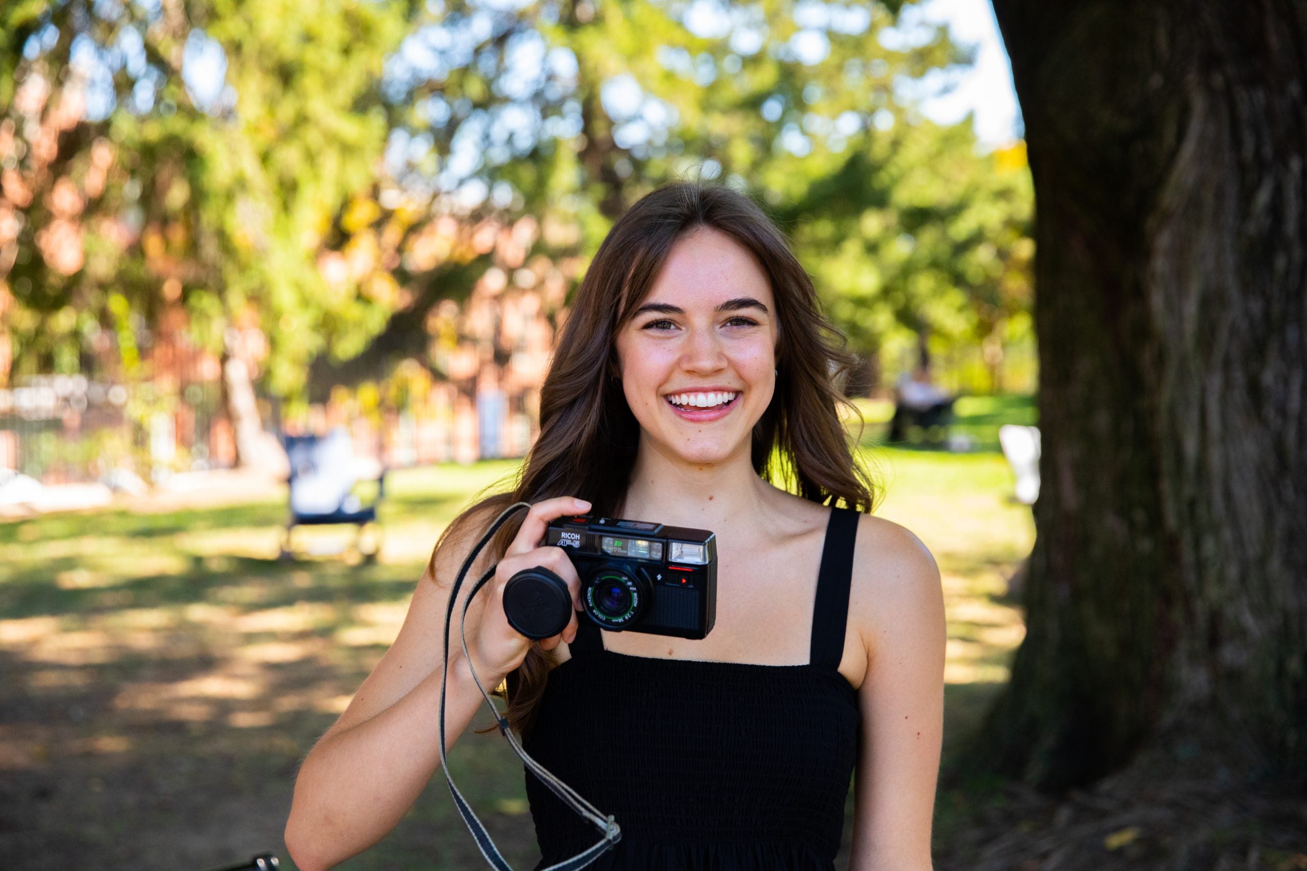 Emma Rose holds a camera outside in front of a tree
