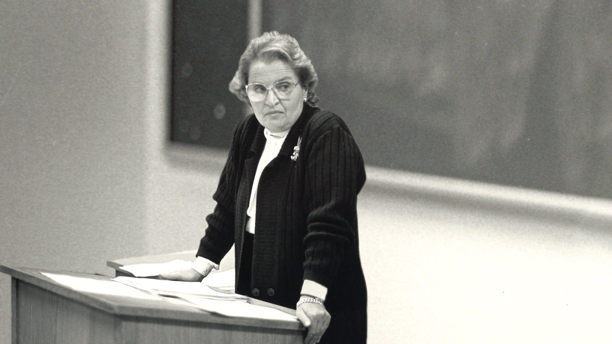 Black and white photo of Madeleine Albright leaning on a podium in front of a chalk board