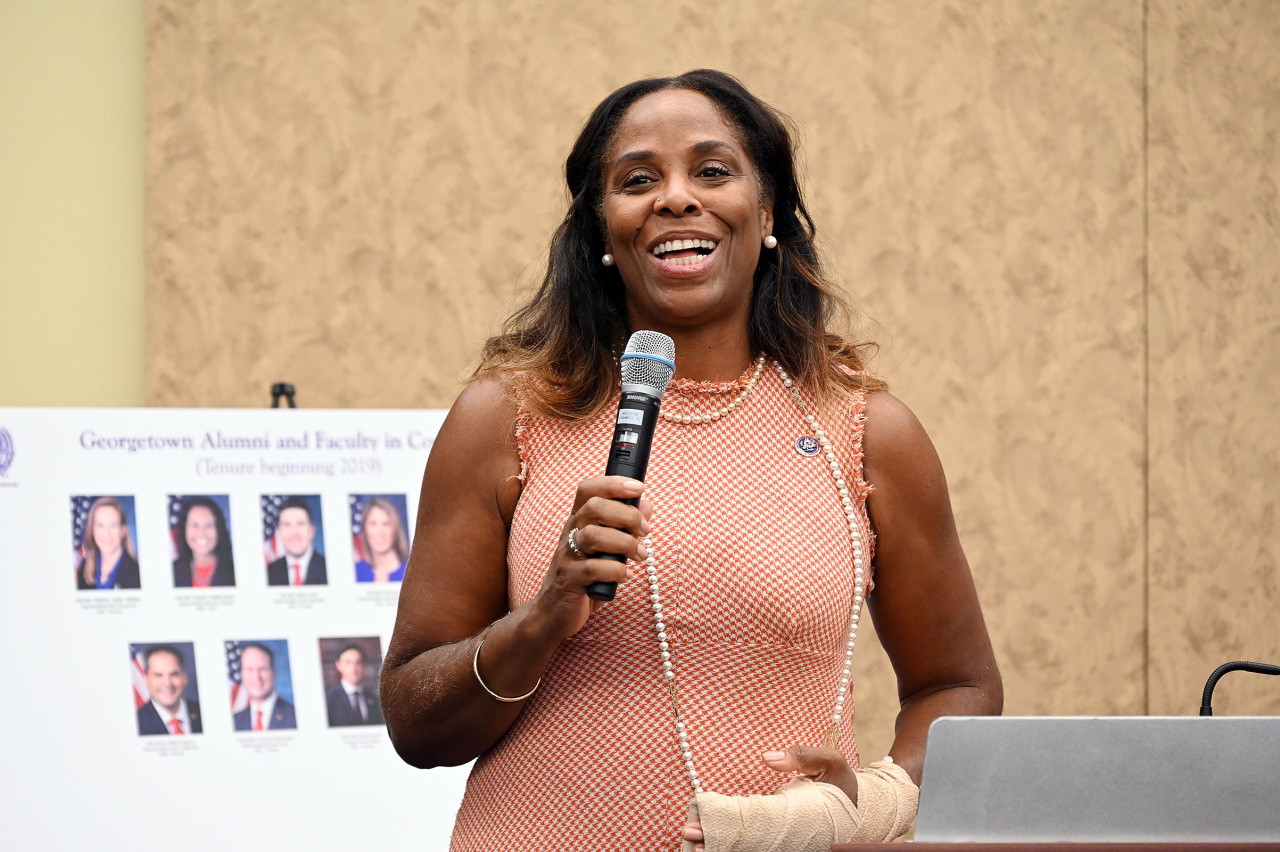 Congresswoman Stacey Plaskett wears a pink dress and bandage on her arm speaks into a microphone