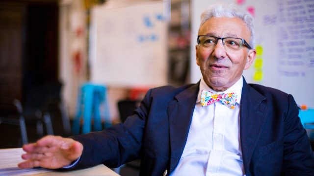 Fathali Moghaddam, a professor in Georgetown's department of psychology, sits at a table talking. He's wearing a suit, patterned bow-tie and glasses.