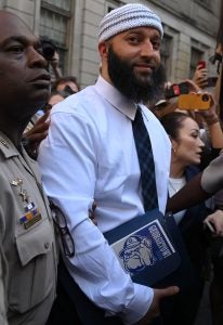 Adnan Syed holds a Georgetown book while being released from prison wearing a collared white shirt and black tie