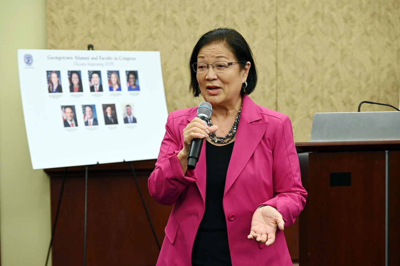 Sen. Mazie Hirono wears a pink blazer and speaks into a microphone
