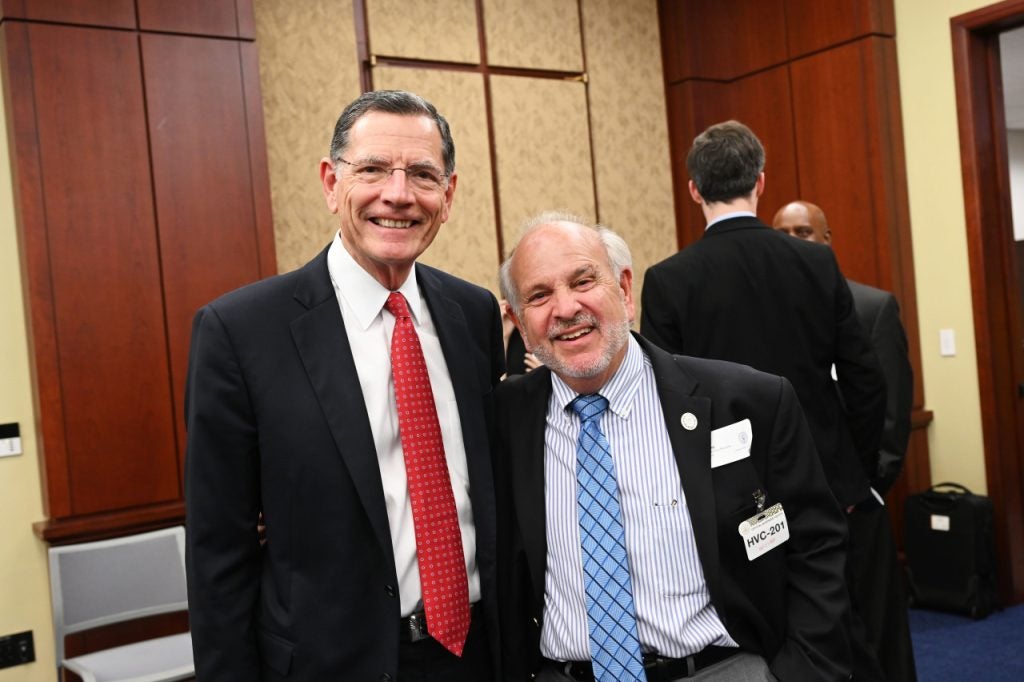 Two men in suits smile at a camera