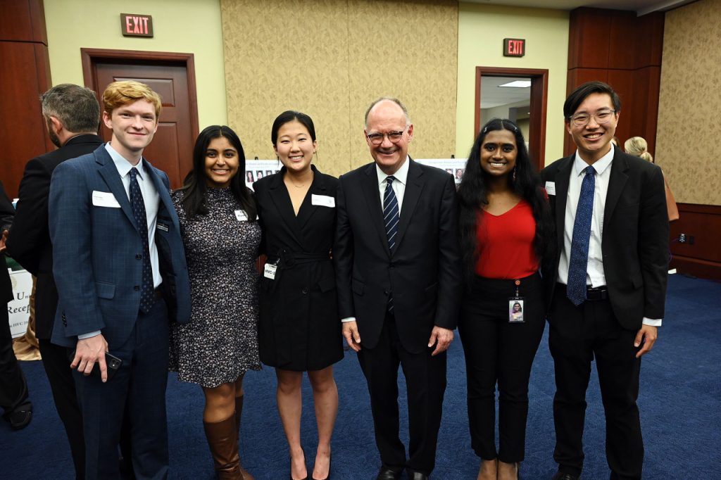 Five students wearing formal clothes stand shoulder to shoulder with Georgetown President John J. DeGioia