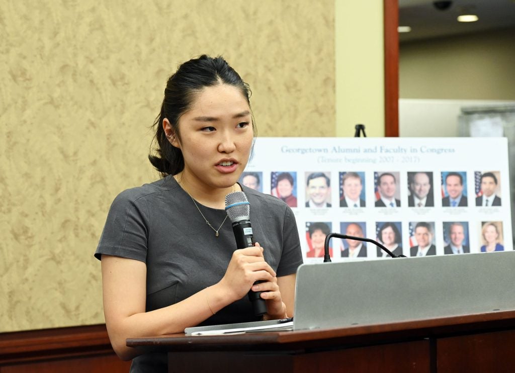 Young woman holds a microphone and speaks from behind a podium