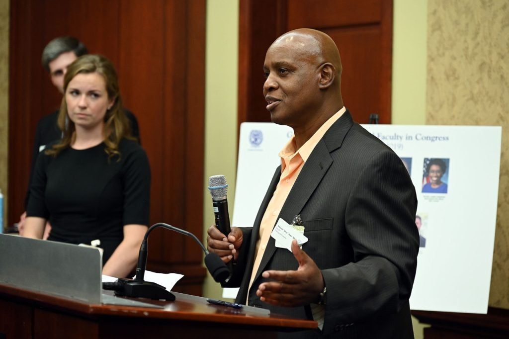 Man holds a microphone as he speaks from behind a podium